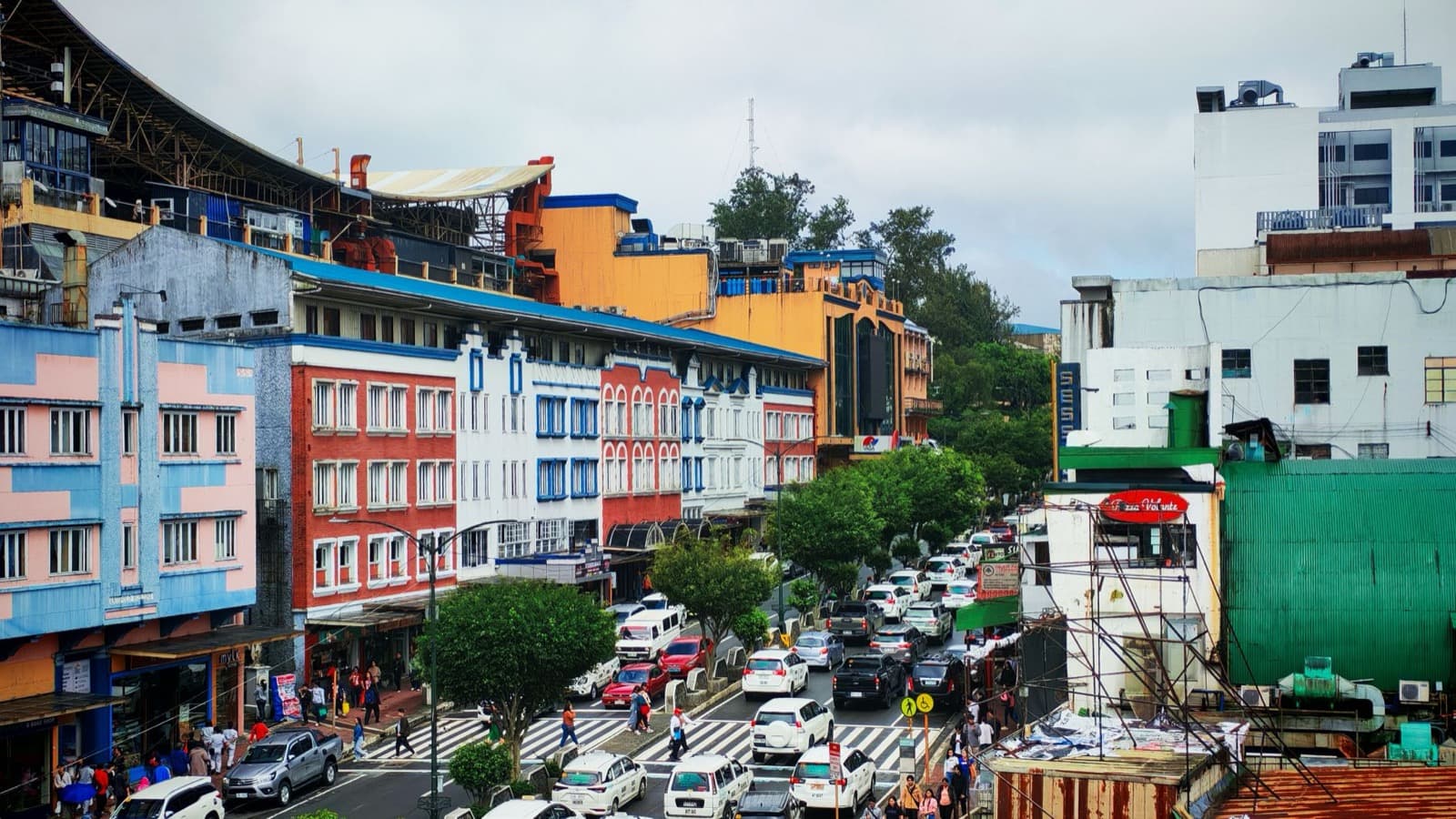 碧瑶市中心 Session Road 一带：彩色外墙的老楼沿坡道排开，路上车流密集，人行道边就是商铺和市场入口